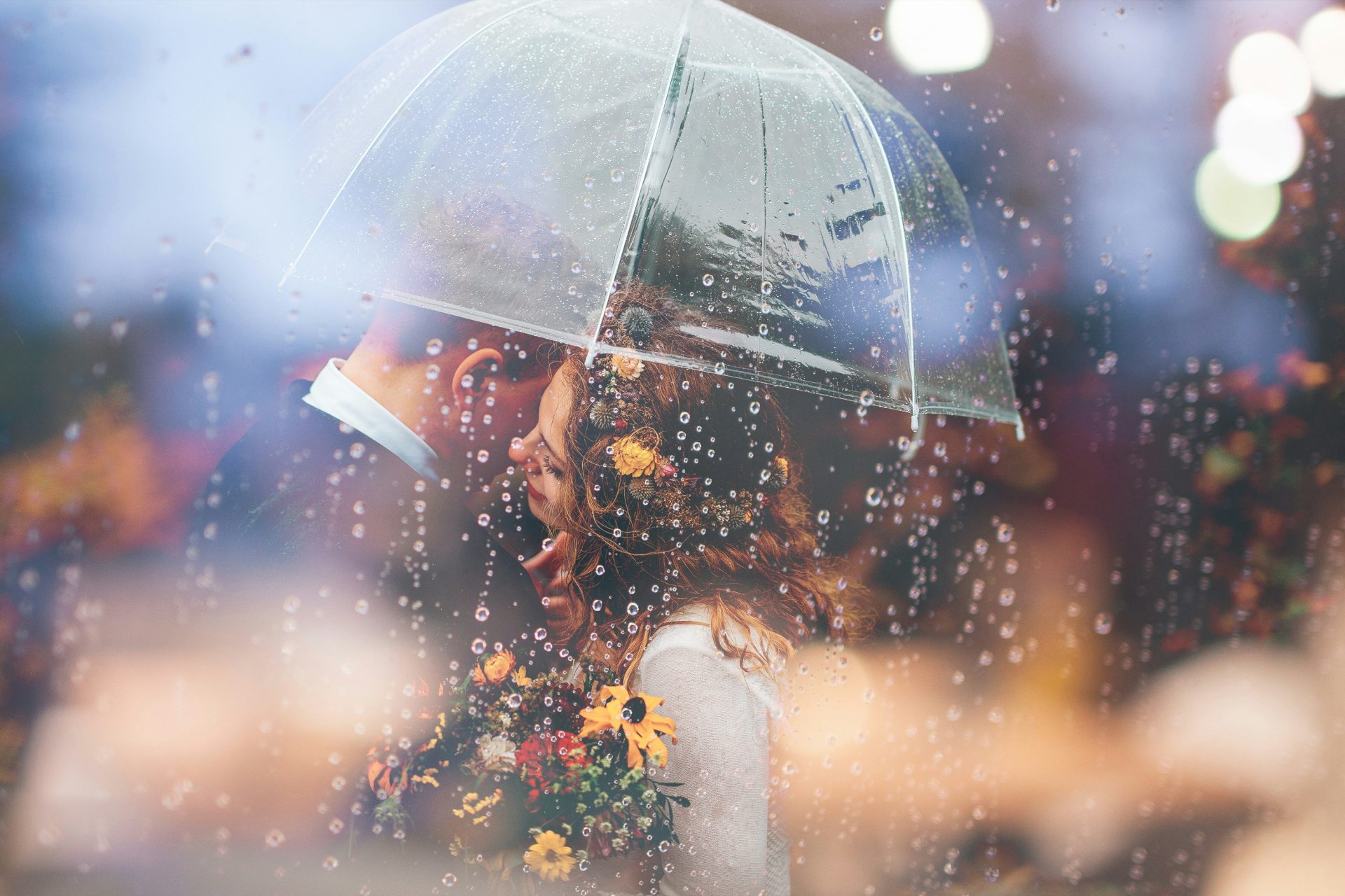 Una novia y un novio se besan bajo la lluvia bajo un paraguas.